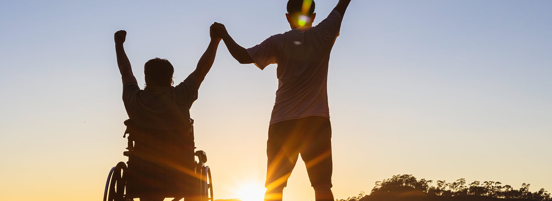 image: Silhouette of joyful disabled man in wheelchair raised hands with friend at sunset